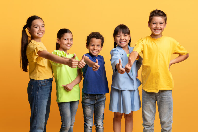 Happy diverse multietnic children showing thumb up, yellow background